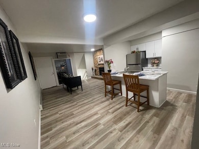Kitchen with white cabinetry, a breakfast bar, light wood-style flooring, a stone fireplace, and freestanding refrigerator