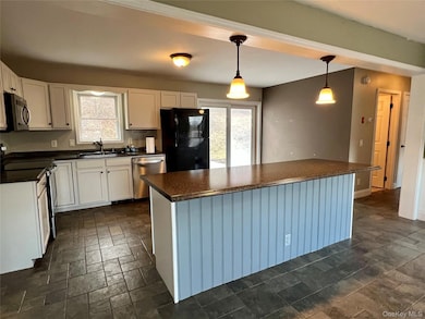 Kitchen featuring stainless steel appliances, pendant lighting, stone tile floors, white cabinetry, and a center island