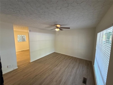 Spare room featuring wood finished floors, plenty of natural light, a textured ceiling, and ceiling fan