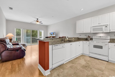 Kitchen featuring white appliances, dark stone counters, white cabinets, open floor plan, and a peninsula