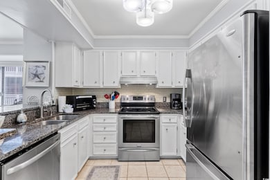 Kitchen featuring stainless steel appliances, a sink, under cabinet range hood, ornamental molding, and white cabinetry