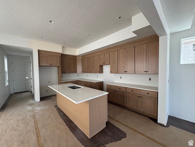 Kitchen with brown cabinetry, a kitchen island with sink, a textured ceiling, concrete floors, and a breakfast bar