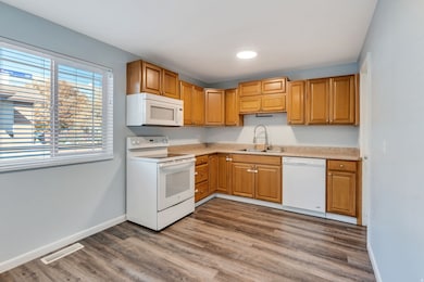 Kitchen featuring white appliances, light countertops, dark wood-style flooring, and brown cabinets