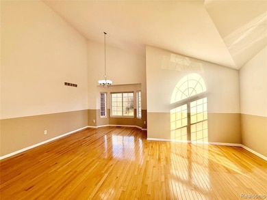 Unfurnished living room with high vaulted ceiling, light wood-style flooring, and a chandelier