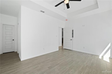 Spare room with a raised ceiling, light wood-type flooring, ceiling fan, and visible vents