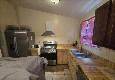 Kitchen featuring stainless steel appliances, wall chimney exhaust hood, light tile patterned floors, and light countertops