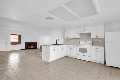 Kitchen featuring white appliances, a peninsula, tasteful backsplash, a glass covered fireplace, and white cabinets