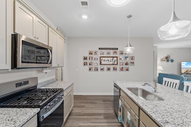 Kitchen with appliances with stainless steel finishes, dark wood-style flooring, decorative light fixtures, and light stone counters