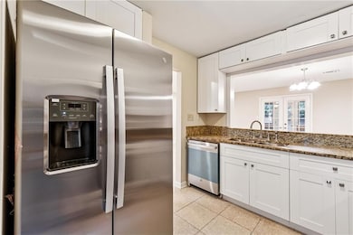 Kitchen featuring appliances with stainless steel finishes, white cabinetry, dark stone counters, and light tile patterned floors