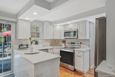 Kitchen with tasteful backsplash, appliances with stainless steel finishes, light wood-type flooring, white cabinets, and recessed lighting