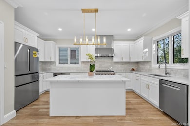 Kitchen featuring crown molding, hanging light fixtures, stainless steel appliances, white cabinets, and light stone counters