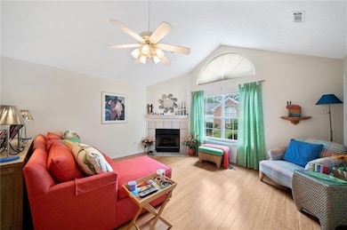 Living area featuring lofted ceiling, wood finished floors, ceiling fan, and a tiled fireplace