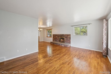 Unfurnished living room featuring a brick fireplace, a chandelier, light wood finished floors, and plenty of natural light