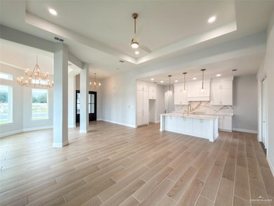 Kitchen featuring open floor plan, white cabinets, a kitchen island with sink, recessed lighting, and a tray ceiling