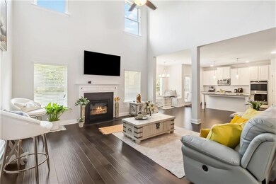 Living area with a fireplace with flush hearth, a towering ceiling, healthy amount of natural light, a ceiling fan, and dark wood-style floors