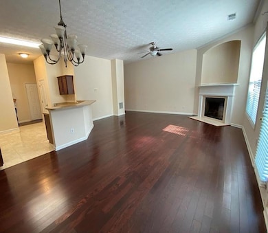 Unfurnished living room with a fireplace with flush hearth, hardwood / wood-style floors, a chandelier, a textured ceiling, and ceiling fan