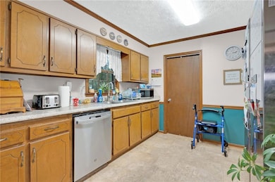 Kitchen featuring stainless steel appliances, crown molding, light countertops, a textured ceiling, and brown cabinetry