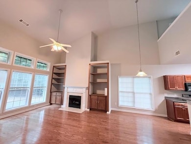 Unfurnished living room with high vaulted ceiling, wood finished floors, a ceiling fan, a fireplace with raised hearth, and baseboards