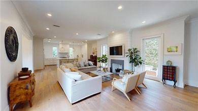 Living room featuring light wood-type flooring, plenty of natural light, recessed lighting, a fireplace, and ornamental molding