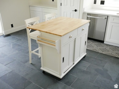 Kitchen with stainless steel dishwasher, white cabinets, butcher block counters, a kitchen bar, and a kitchen island