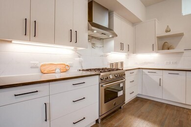 Kitchen featuring high end stainless steel range, wall chimney range hood, white cabinets, open shelves, and dark wood-style flooring