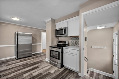 Kitchen with appliances with stainless steel finishes, white cabinets, light countertops, dark wood-style flooring, and crown molding