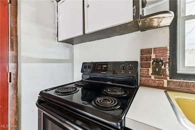 Kitchen with black range with electric cooktop, white cabinetry, and light countertops