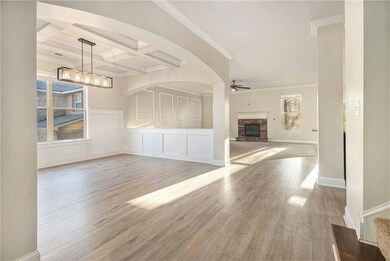 Unfurnished living room with a ceiling fan, a stone fireplace, a chandelier, wood finished floors, and crown molding