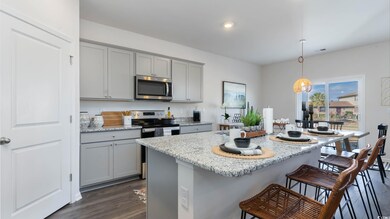 Virtually staged Kitchen with stainless steel appliances, gray cabinets, a kitchen breakfast bar, dark wood-style flooring, and light stone counters