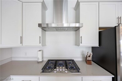 Kitchen featuring wall chimney exhaust hood, appliances with stainless steel finishes, white cabinetry, and light stone counters