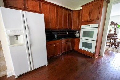 Kitchen with white appliances, dark wood-type flooring, dark countertops, tasteful backsplash, and brown cabinets