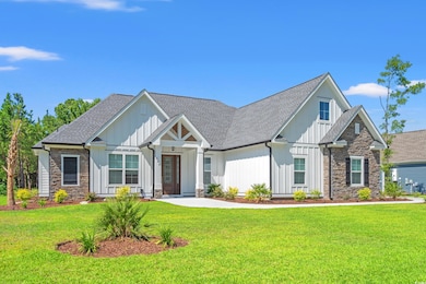 View of front of home with stone siding, a front yard, roof with shingles, and board and batten siding