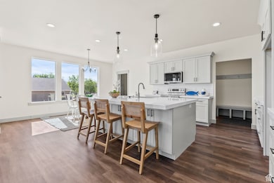 Kitchen with decorative backsplash, decorative light fixtures, a kitchen breakfast bar, white cabinetry, and a kitchen island with sink