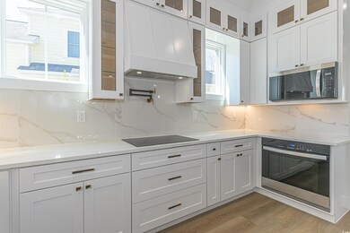 Kitchen with light wood-style flooring, light stone countertops, custom exhaust hood, stainless steel appliances, and white cabinetry