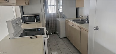 Kitchen featuring light countertops, electric stove, light tile patterned flooring, stainless steel microwave, and light brown cabinets