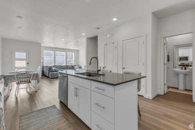 Kitchen featuring wood finished floors, dark countertops, white cabinets, an island with sink, and a textured ceiling