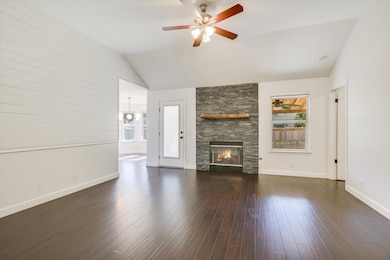 Unfurnished living room featuring a stone fireplace, plenty of natural light, vaulted ceiling, and dark wood finished floors