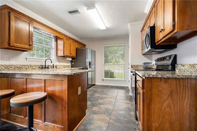 Kitchen with stainless steel appliances, light stone counters, plenty of natural light, brown cabinetry, and crown molding