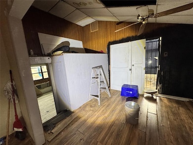 Unfurnished room with wood-type flooring, wood walls, a drop ceiling, lofted ceiling, and ceiling fan