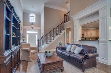 Another view of the living room showcasing the grand staircase with wrought iron spindles, two story ceilings and exquisite woodworking.