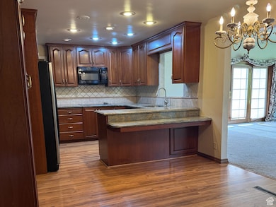Kitchen featuring a peninsula, tasteful backsplash, decorative light fixtures, black microwave, and freestanding refrigerator