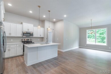Kitchen with white cabinets, stainless steel appliances, a center island with sink, recessed lighting, and decorative light fixtures