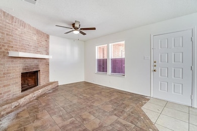 Unfurnished living room with a textured ceiling, a brick fireplace, tile patterned floors, and a ceiling fan