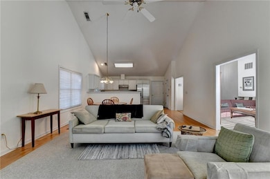 Living room featuring high vaulted ceiling, a ceiling fan, light wood-type flooring, and a chandelier