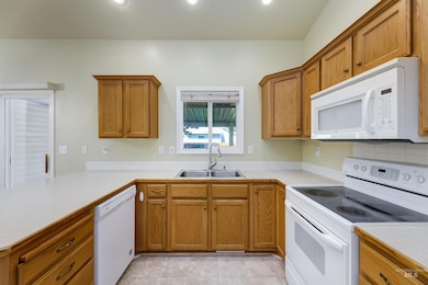 Kitchen featuring white appliances, light countertops, brown cabinetry, recessed lighting, and a peninsula