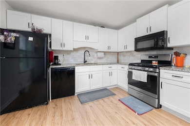 Kitchen with black appliances, a sink, white cabinetry, light wood-style flooring, and light stone counters