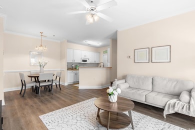 Living room with dark wood finished floors, crown molding, a ceiling fan, and a chandelier