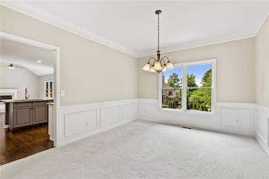 Spare room with a chandelier, dark colored carpet, wainscoting, crown molding, and ceiling fan
