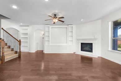 Unfurnished living room with built in shelves, a glass covered fireplace, dark wood-style floors, ceiling fan, and recessed lighting