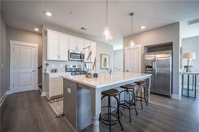 Kitchen with appliances with stainless steel finishes, dark wood finished floors, a sink, a kitchen island with sink, and light countertops